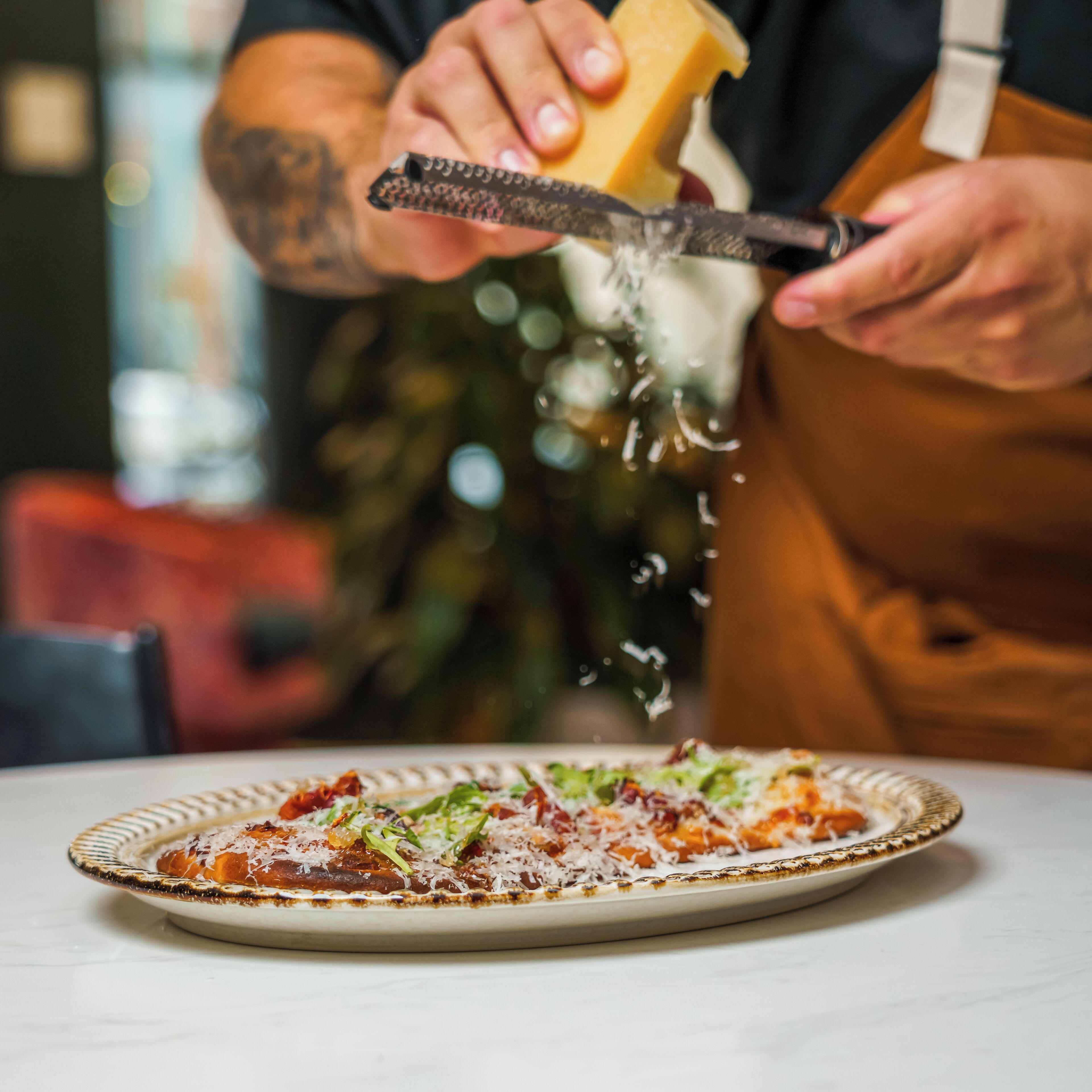Una persona rallando queso sobre una pizza en un plato.