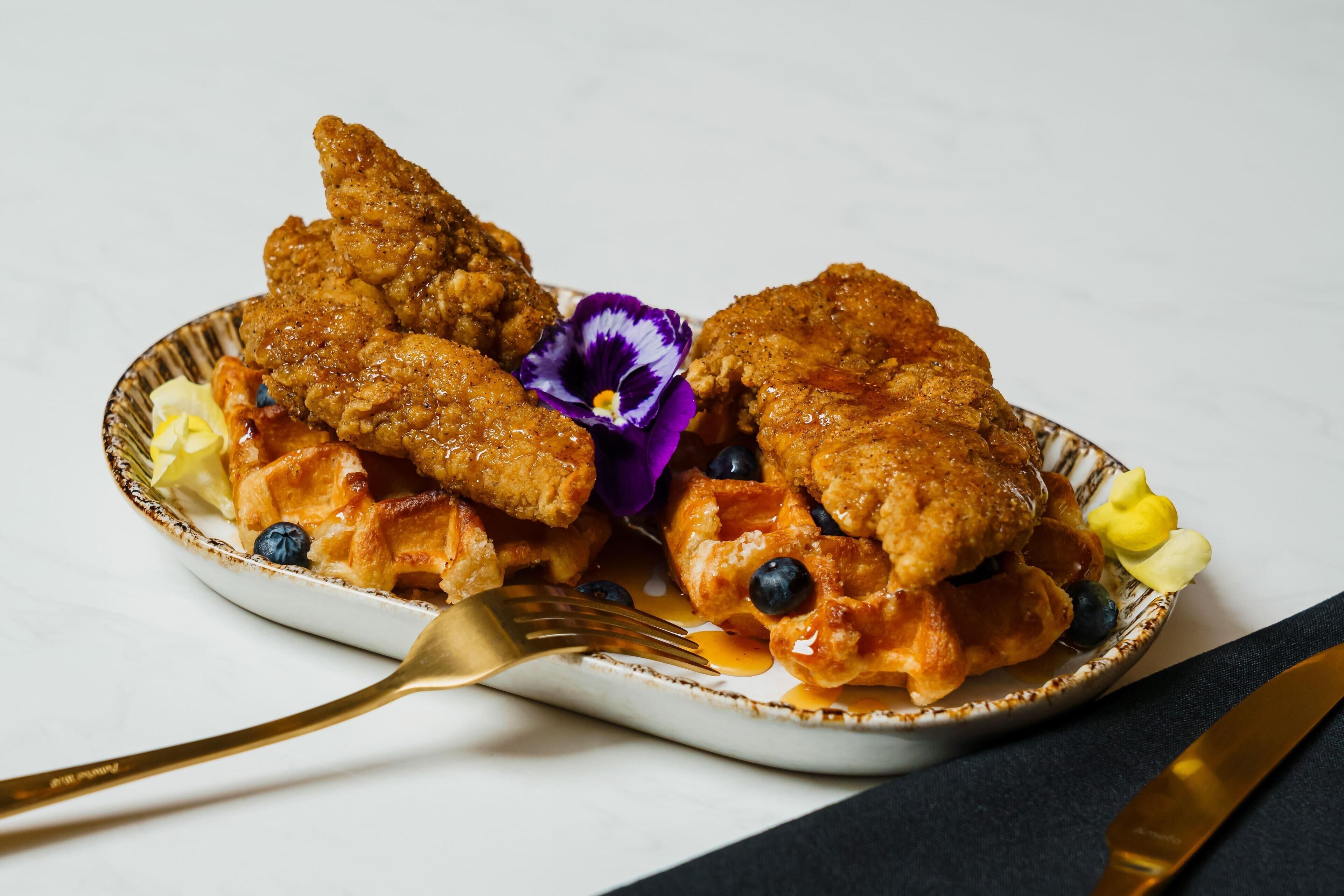 Une assiette contenant du poulet frit, des gaufres, des myrtilles et une fleur.