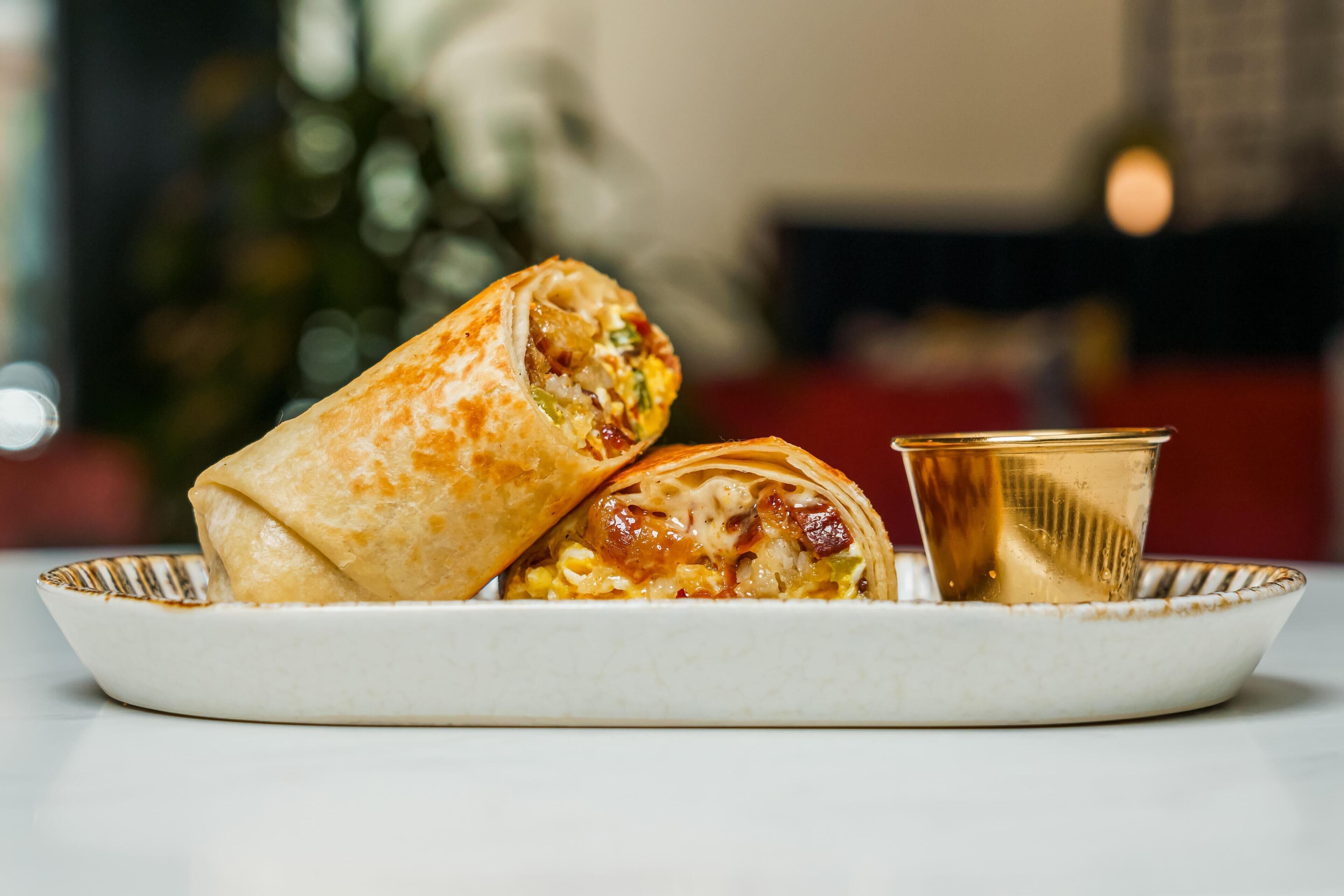 A plate with two burritos and a glass of beverage.