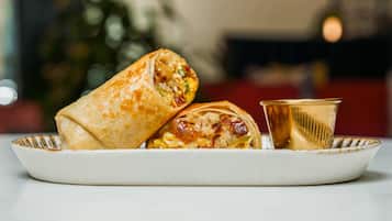A plate with two burritos and a glass of beverage.