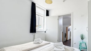 Ein Hotelzimmer mit zwei Betten, einem Vorhangfenster, einer Pendelleuchte und einem kleinen Hocker mit einer Pflanze.