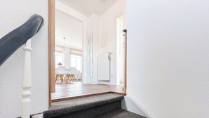 Eine Treppe führt zu einem Raum mit einer weißen Tür, einem Heizkörper und einem Essbereich mit Stühlen und einem Tisch.