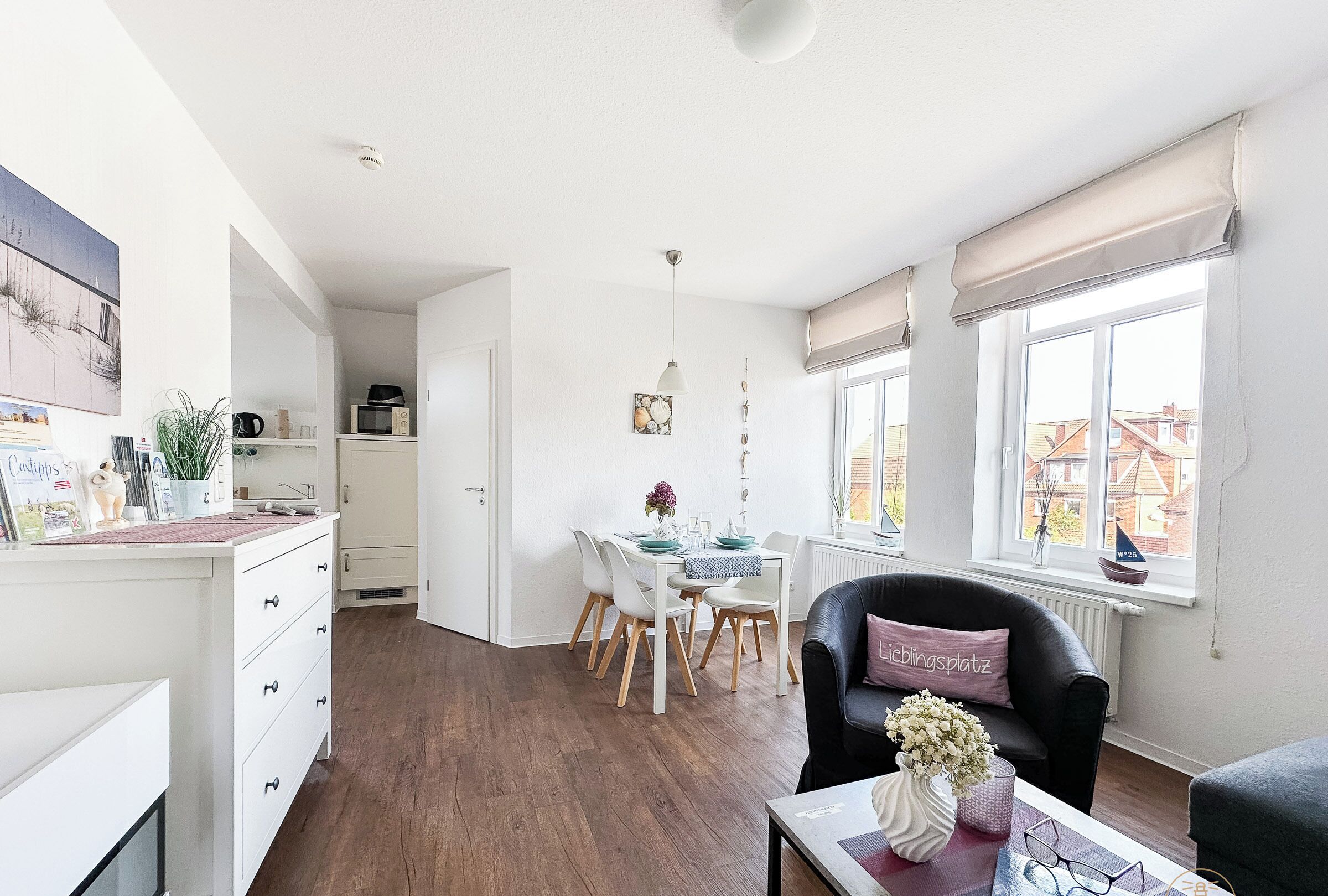 Une cuisine moderne avec des meubles blancs, un coin repas doté d’une table et de chaises blanches, et un fauteuil en cuir noir avec un coussin.