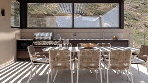 Een eethoek buiten met een tafel, stoelen, een barbecue en uitzicht op het omliggende landschap.