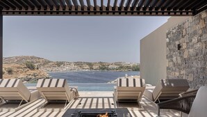 Een terras buiten met lounge fauteuils, een vuurkorf en uitzicht op zee en heuvels.