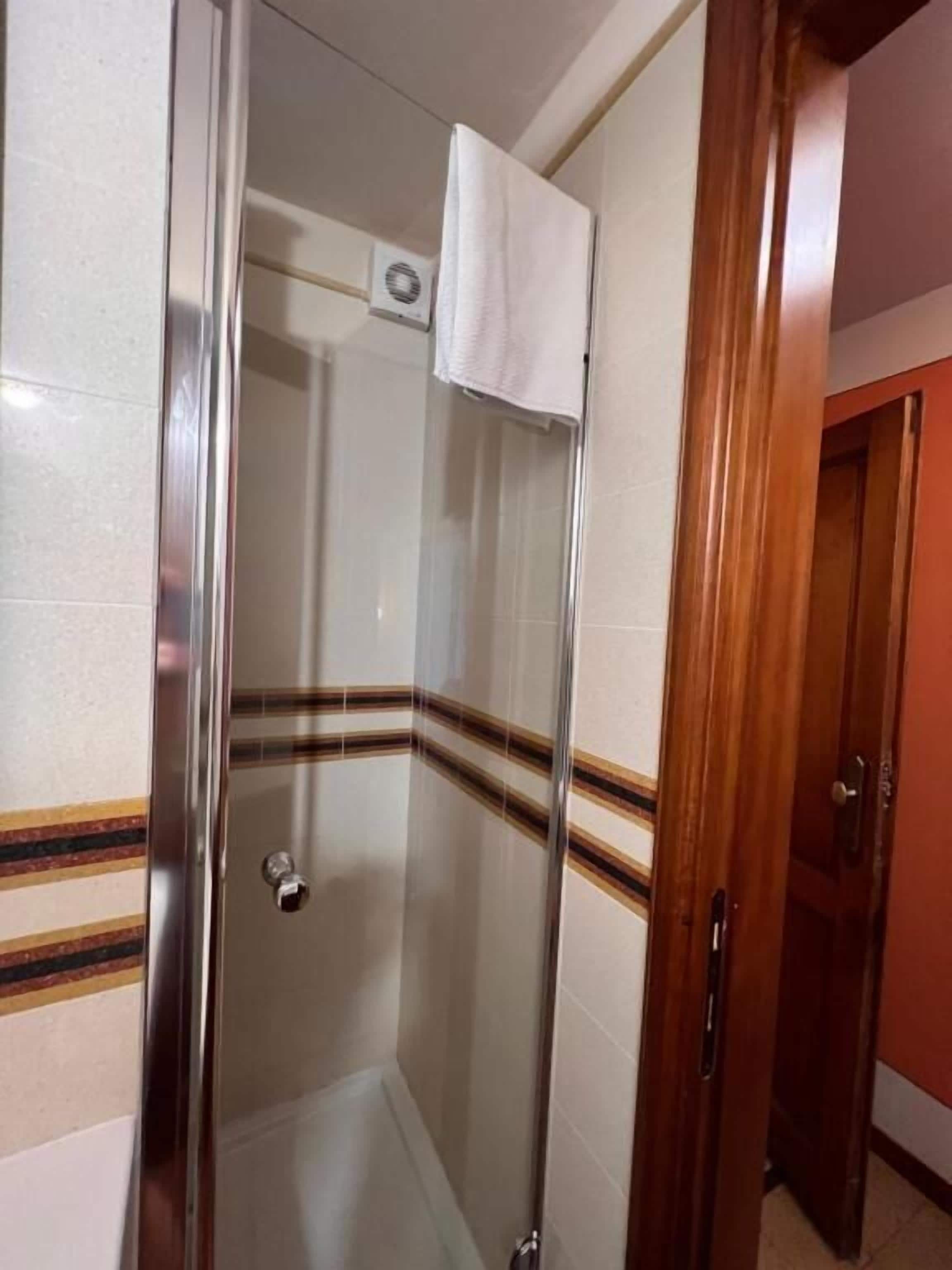 A glass-enclosed shower stall with a towel hanging on the wall, a door with a handle, and a tiled floor.