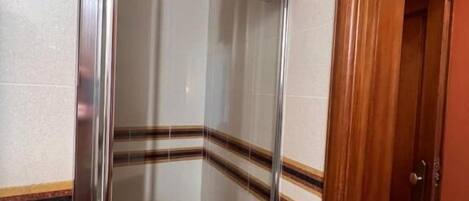 A glass-enclosed shower stall with a towel hanging on the wall, a door with a handle, and a tiled floor.