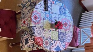 A round table with a colorful patterned tablecloth, surrounded by white chairs with cushioned seats. - Tosca (Florence)