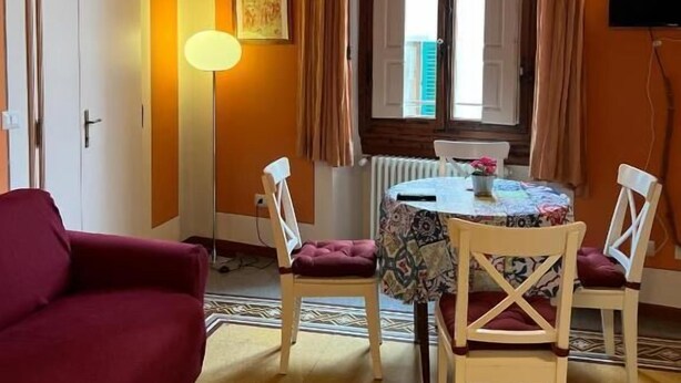 A room with a dining table, chairs, a sofa, a lamp, a TV, and a window with curtains. - Tosca (Florence)