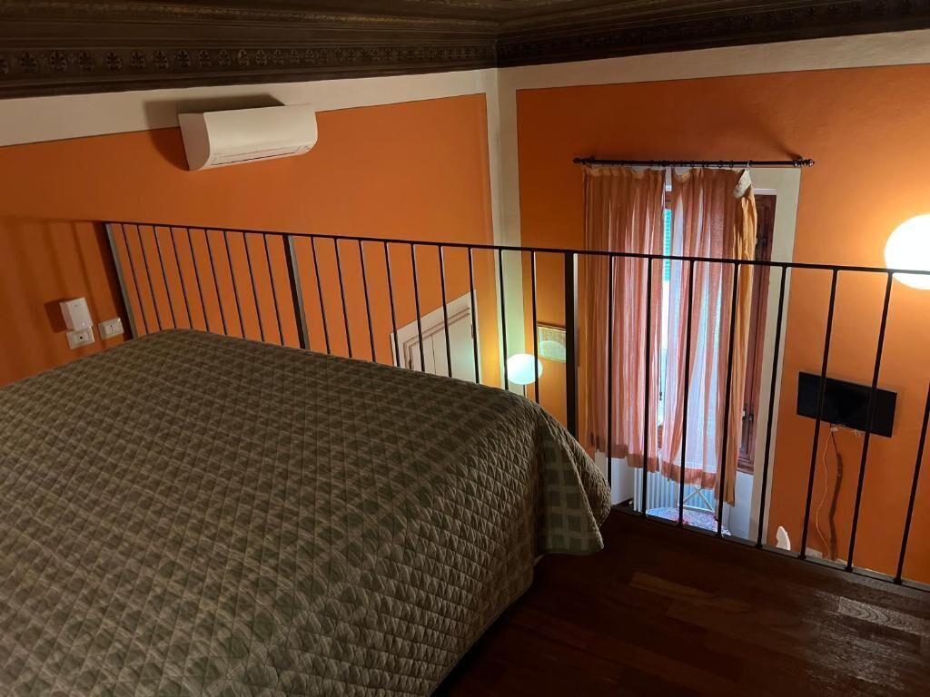 Ein Zimmer mit einem Bett, einem Vorhangfenster, einer wandmontierten Klimaanlage und einer Treppe.