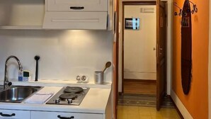 A kitchen with white cabinets, a sink, and a stove. There is a hallway with an orange wall and a door leading to another room. - Tosca (Florence)