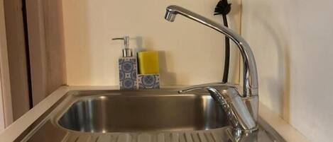 A stainless steel kitchen sink with a modern faucet, a soap dispenser, and a yellow sponge on the countertop.
