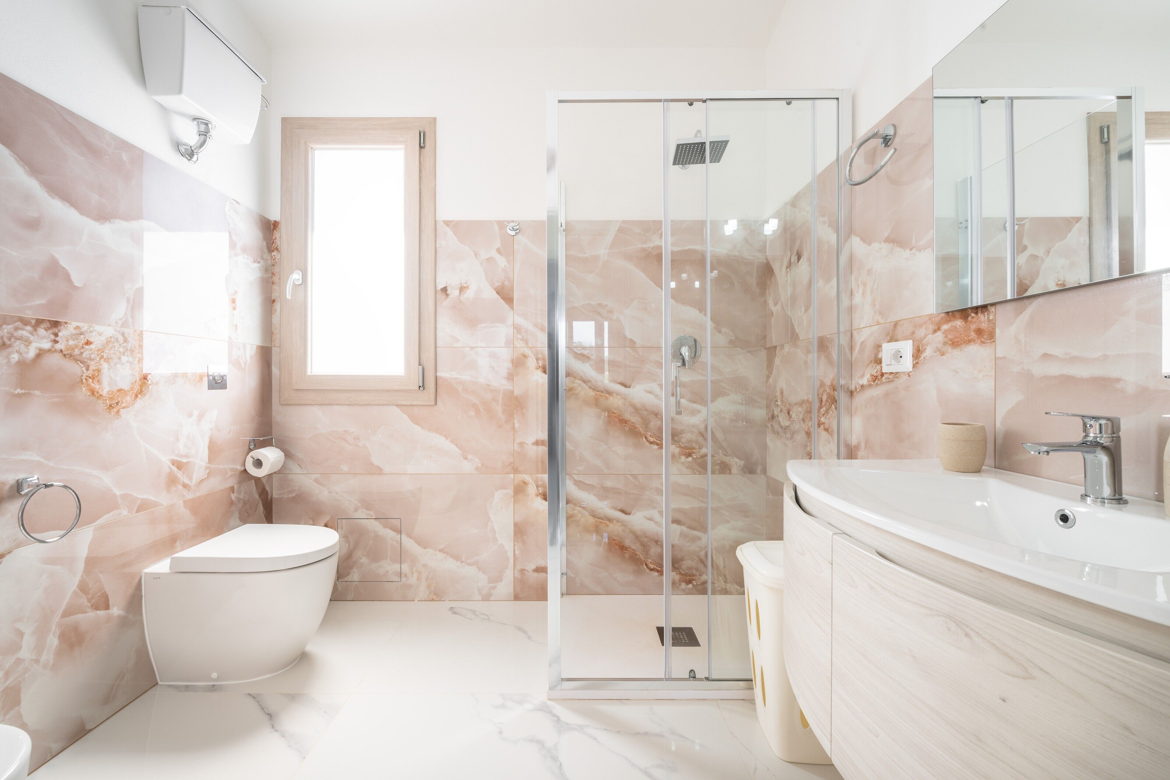 A bathroom with a marble wall, a toilet, a shower enclosure, and a vanity with a mirror.
