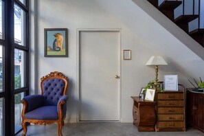 A room with a large window, a door, a blue upholstered chair, a wooden cabinet, and a framed picture on the wall. - Naptel Changmoi (Chiang Mai)