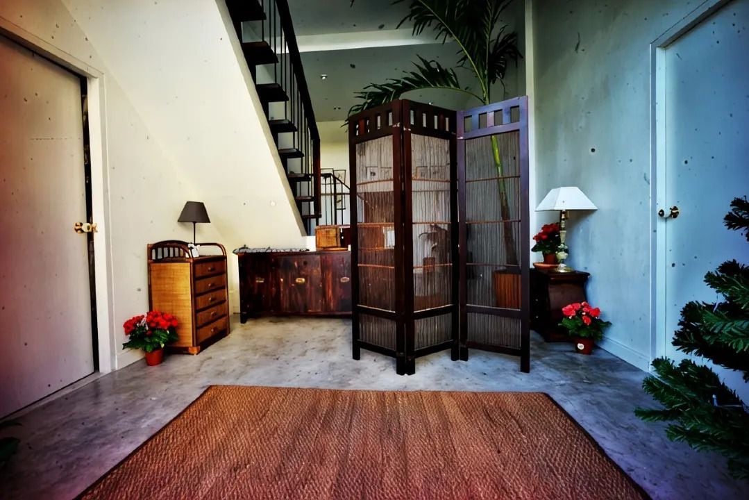 A staircase leading to an upper floor, a wooden cabinet with drawers, a small table with a lamp, and a potted plant.