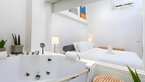 A modern hotel room with a large bathtub, a bed with white linens, a bedside table with a lamp, and a potted plant. - Naptel Changmoi (Chiang Mai)
