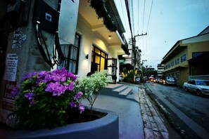 A street view with a building featuring a large planter with flowers, a visible entrance, and a sidewalk. - Naptel Changmoi (Chiang Mai)