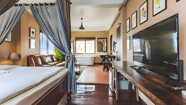 A hotel room with a bed, a TV, a desk, a bathroom, and a window with a view. - Naptel Changmoi (Chiang Mai)