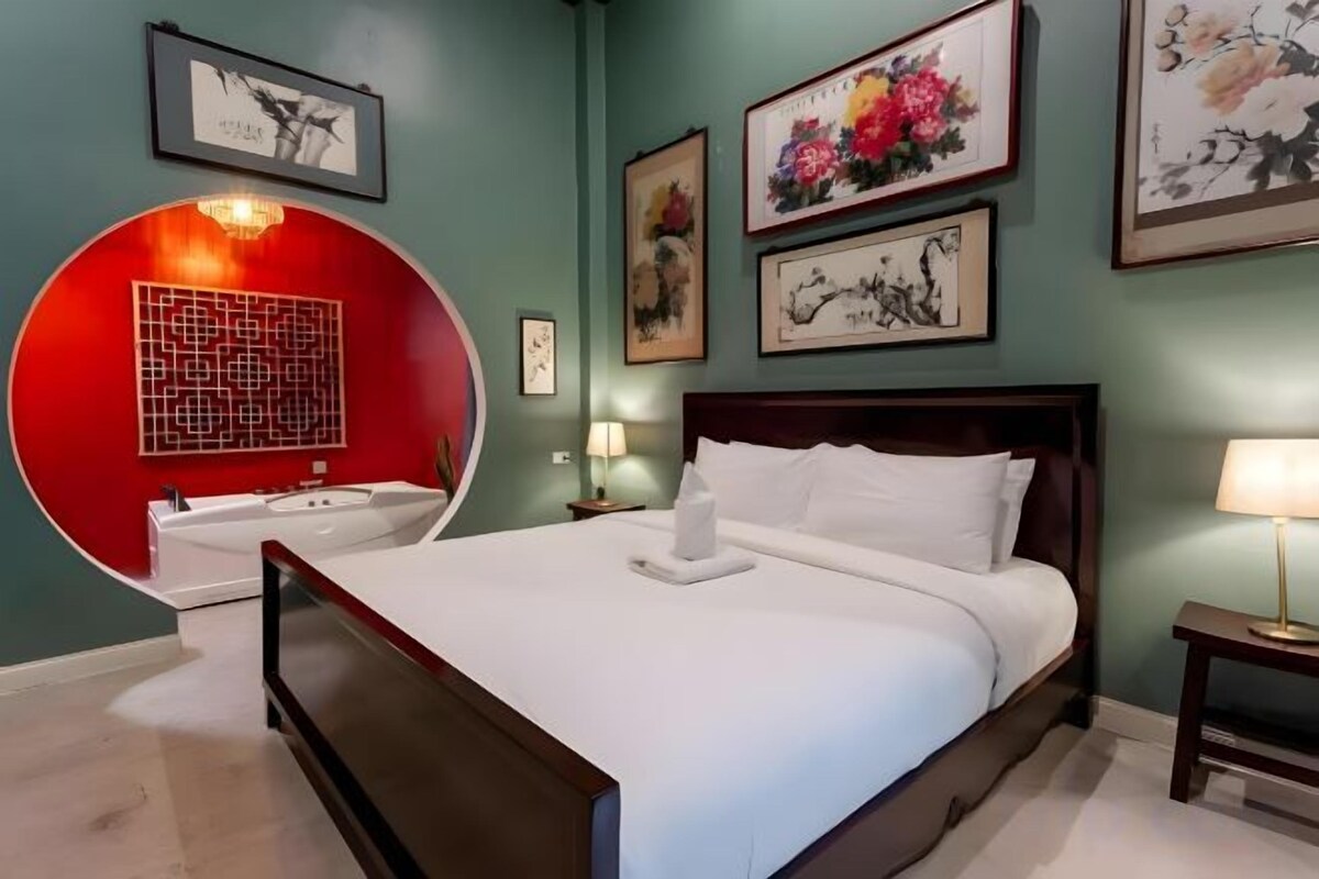 A bedroom with a bed, bedside tables, a red circular wall feature, and framed artwork on the walls.