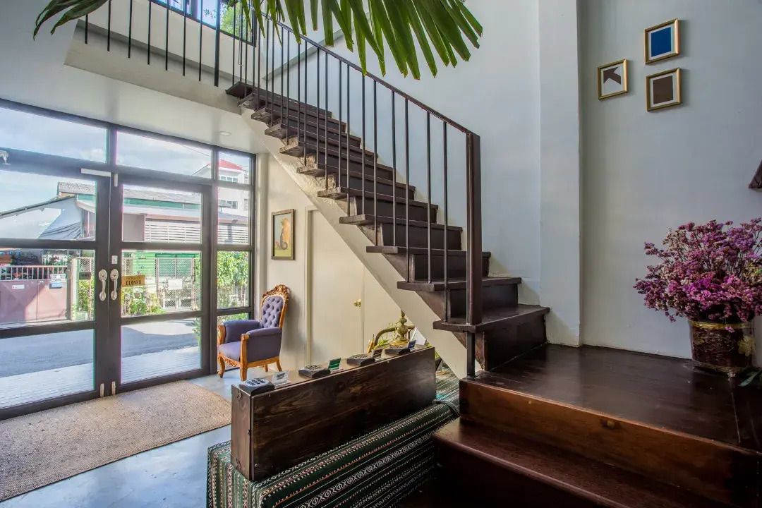 A staircase with a metal railing leading to a landing, a chair, and a potted plant.