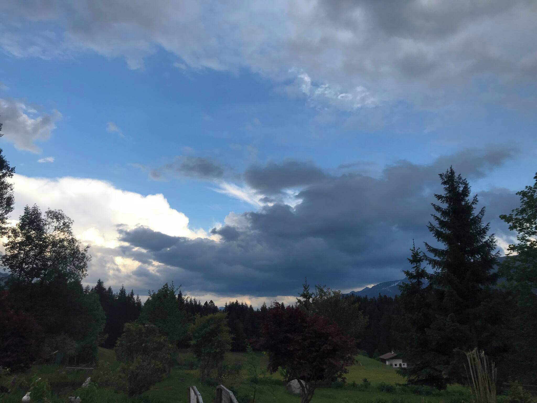 A rural landscape with a house, trees, and a cloudy sky.