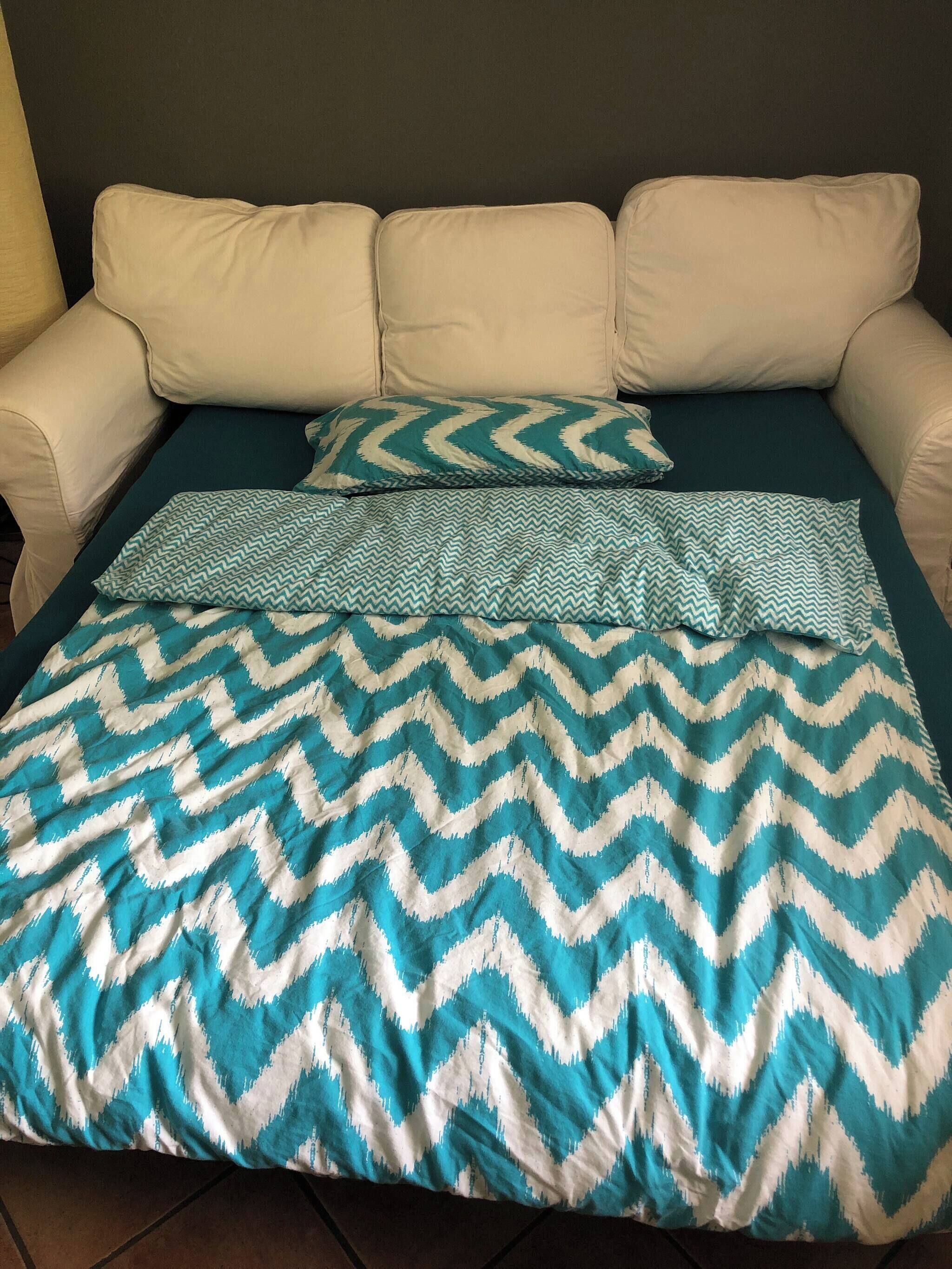 Een bed met een bedsprei met een patroon, een beige bank en een donkere muur.