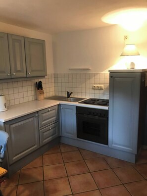 Une cuisine avec des meubles blancs, une cuisinière, un évier et un pare-feu en carreaux.