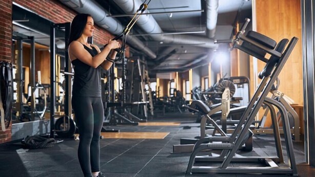 A gym with exercise equipment, a person using a cable machine, and a bench press. - The Lawrence Hotel Lawrenceville, Tapestry Collection Hilton (Lawrenceville)
