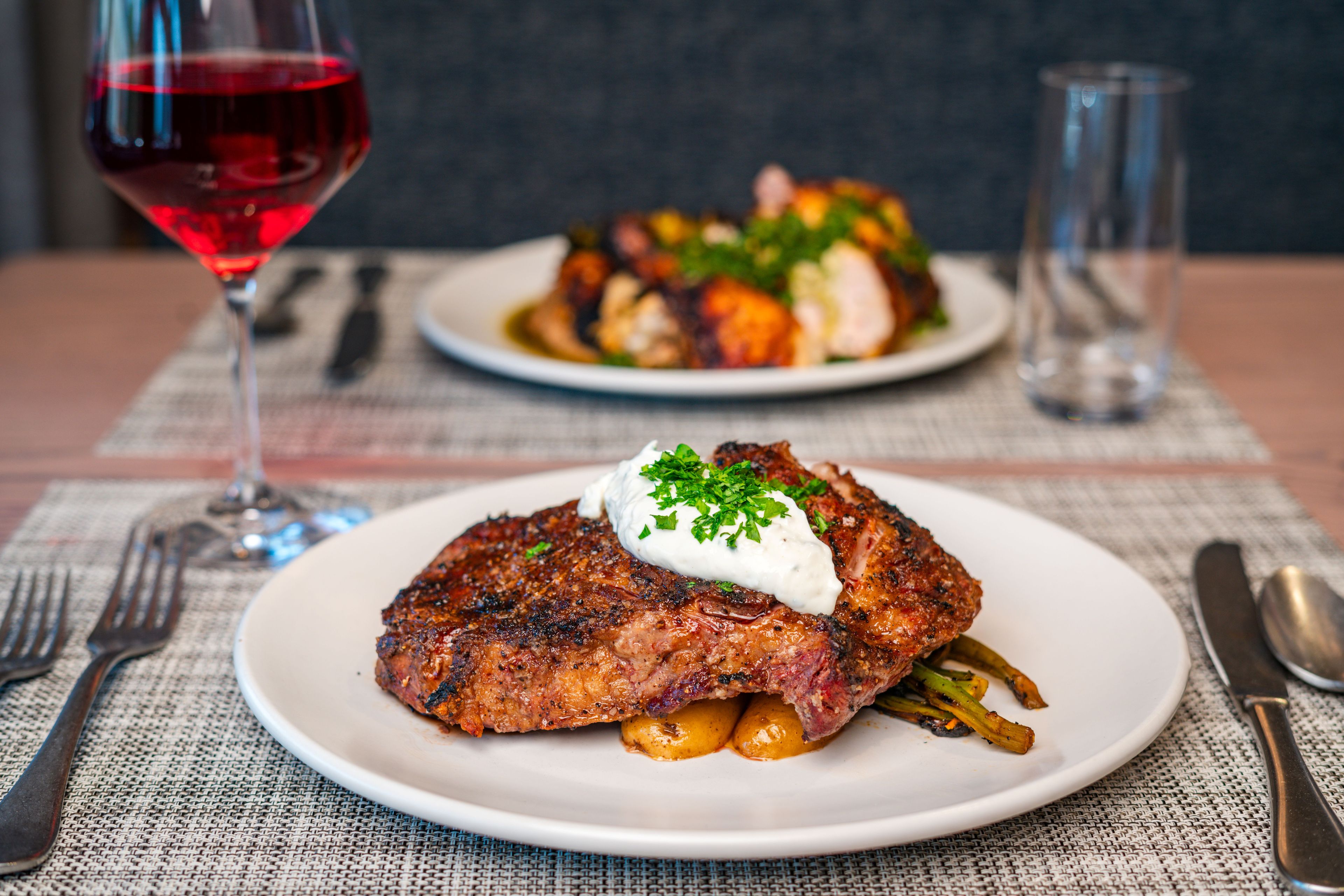Prato de comida com bife e legumes, um copo de vinho tinto e talheres sobre uma toalha de mesa.