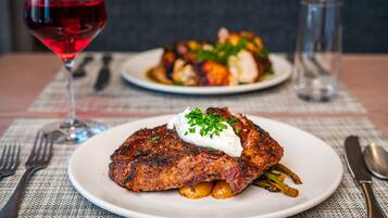 Prato de comida com bife e legumes, um copo de vinho tinto e talheres sobre uma toalha de mesa.