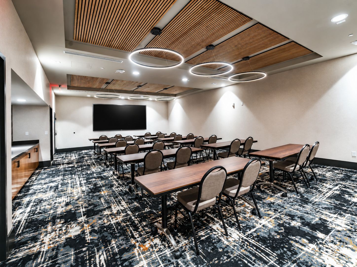 Un salón de conferencias con una pantalla plana grande, varias mesas y sillas.