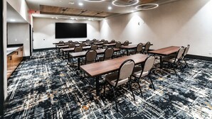 A conference room with a large flat-screen TV, multiple tables, and chairs. - The Lawrence Hotel Lawrenceville, Tapestry Collection Hilton (Lawrenceville)