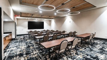 Un salón de conferencias con una pantalla plana grande, varias mesas y sillas.