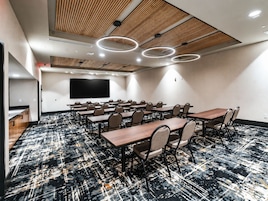 Un salón de conferencias con una pantalla plana grande, varias mesas y sillas.