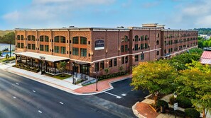 A multi-story hotel with a brick facade, a covered outdoor seating area, and a parking lot. - The Lawrence Hotel Lawrenceville, Tapestry Collection Hilton (Lawrenceville)