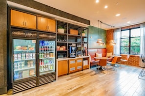 Une chambre d’hôtel équipée d’une kitchenette, d’un coin salon avec une table et des chaises, et d’une grande fenêtre donnant sur la forêt.