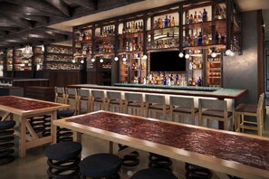 A bar area with multiple seating options, a bar counter, and shelves stocked with various bottles.