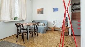 A room with a dining table, chairs, a blue sofa, a window with curtains, a red ladder, and a kitchen area with shelves. - RentPlanet - przy Placu Zbawiciela (Warsaw)