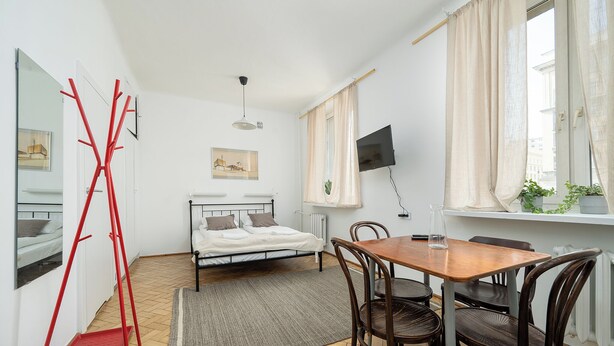 A bedroom with a bed, bedside table, and a TV on the wall. - RentPlanet - przy Placu Zbawiciela (Warsaw)