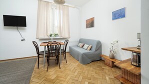A room with a dining table, chairs, a sofa, a TV mounted on the wall, a window with curtains, and a wooden floor. - RentPlanet - przy Placu Zbawiciela (Warsaw)