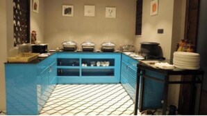 Un coin cuisine avec un plan de travail bleu, un sol carrelé et un mur orné de tableaux encadrés.