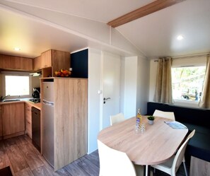 A compact kitchen with wooden cabinets, a built-in fridge, and a dining area with a table and chairs. - COTTAGE PARKS LA FORÊT - 3 bed 6 bath mobile home in the heart of the chateau park (Saint-Julien-des-Landes)