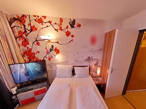 A hotel room with a bed, a TV, a wall mural, and a nightstand with a lamp. - Studio Rainer mit Pool und Sauna (Freyung)