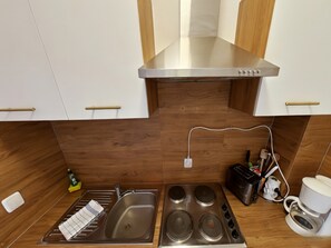 Eine Küche mit Dunstabzugshaube aus Edelstahl, einer Spüle mit Geschirrgestell, einem Kochfeld und einer Kaffeemaschine.