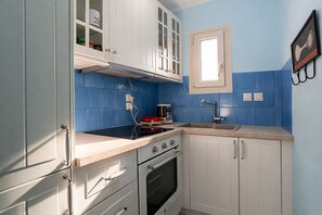 A kitchen with white cabinets, a black stove, a sink, and blue-tiled walls.