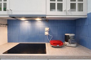 A kitchen with a black induction cooktop, a red electric kettle, and a coffee maker on the counter.