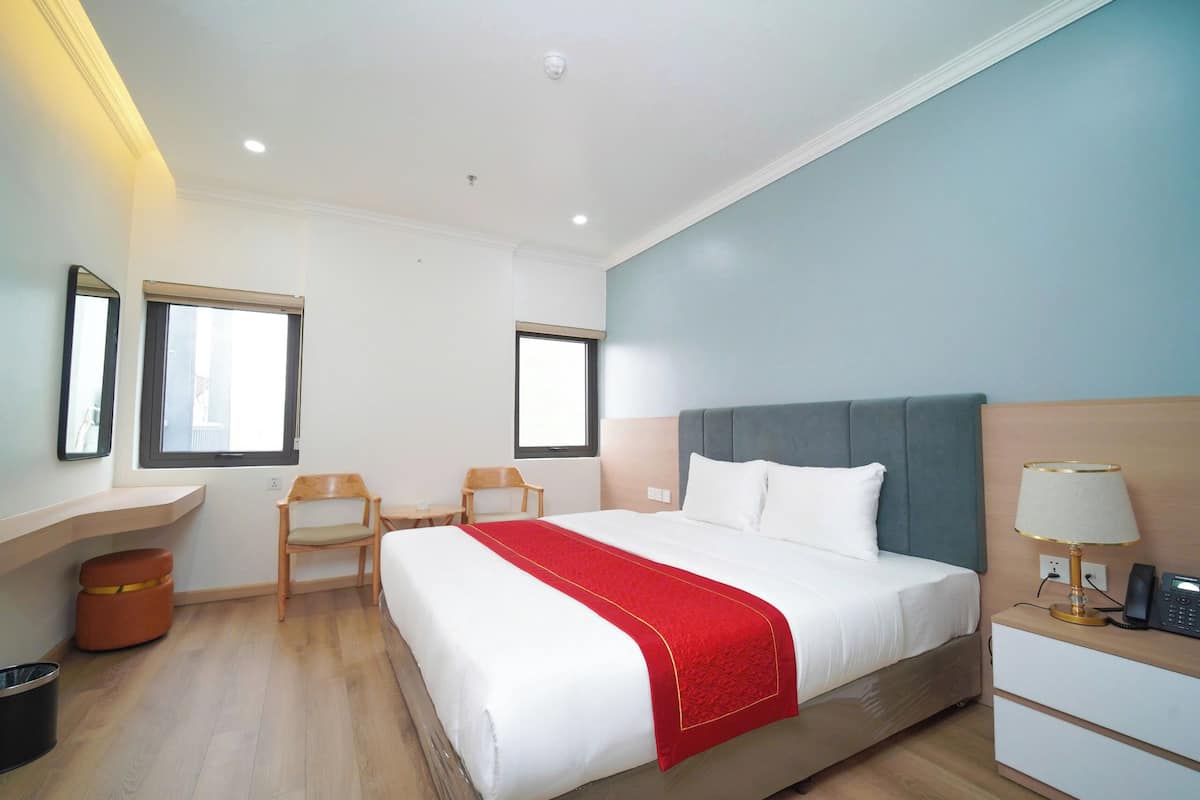 Een hotelkamer met een bed, een bureau, een stoel en een nachtkastje met een lamp.