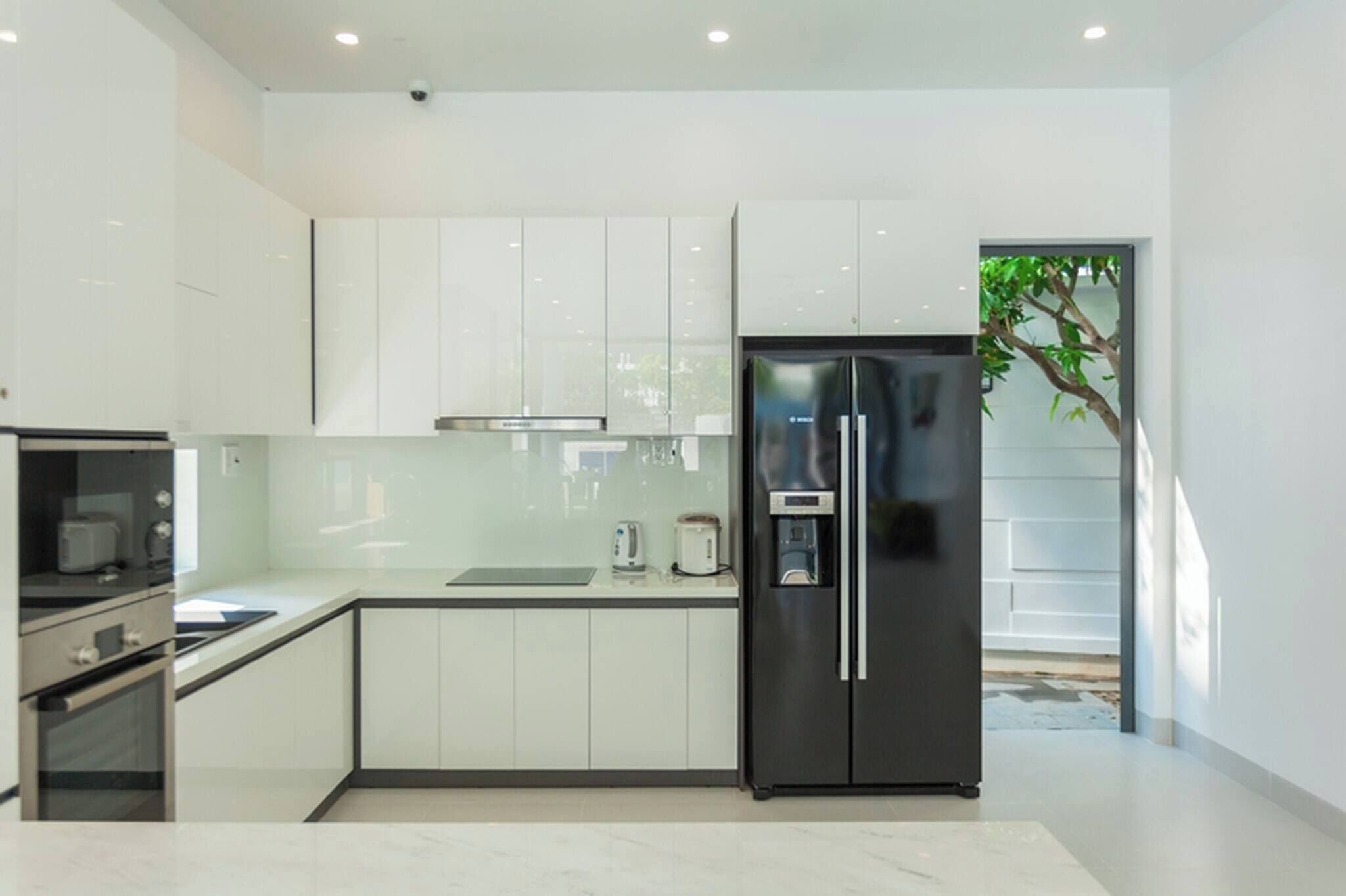 A modern kitchen with white cabinets, a black refrigerator, and a visible tree outside.
