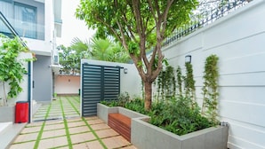Une cour moderne avec un chemin pavé, un arbre et une entrée fermée par un portail.