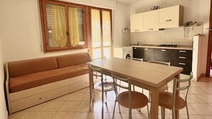 Un espacio habitable compacto con sofá, mesa de comedor, sillas, kitchenette y una ventana con cortinas.